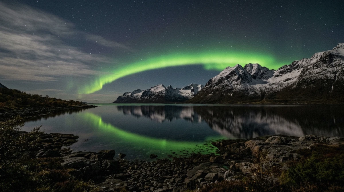 Green aurora arc over a still fjord and snow-covered peaks at a viewing stop on a Tromso Northern Lights tour, Troms county, Norway