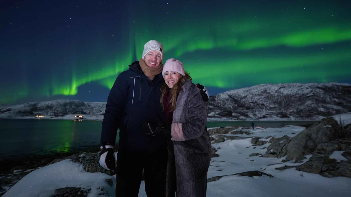 Minibus parked on a snowy inland road under a bright aurora during a cross-border Tromso Northern Lights tour toward Finland